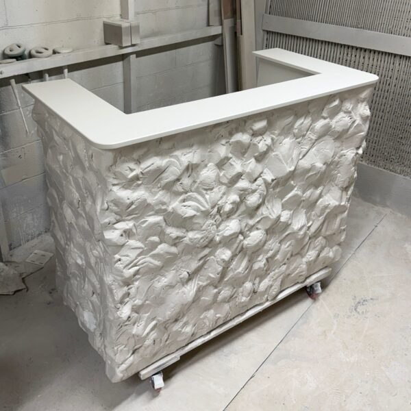 A stylish, modern reception desk or bar counter with a textured white stone-like front and a smooth white countertop