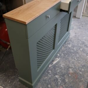 Bespoke sage green radiator cover with integrated storage drawer and solid oak top in a workshop.