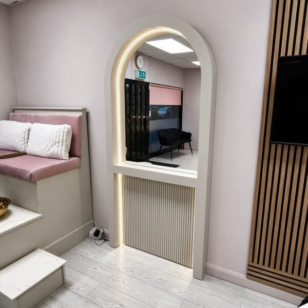 Curved mirror with reeded base and warm LED halo lighting featuring a tall arched design and slim profile.