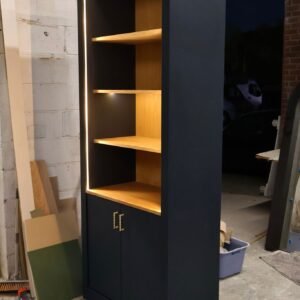 Modern display bookcase with solid natural grain oak shelves contrasted by a deep navy-painted cabinet and warm LED halo lighting.