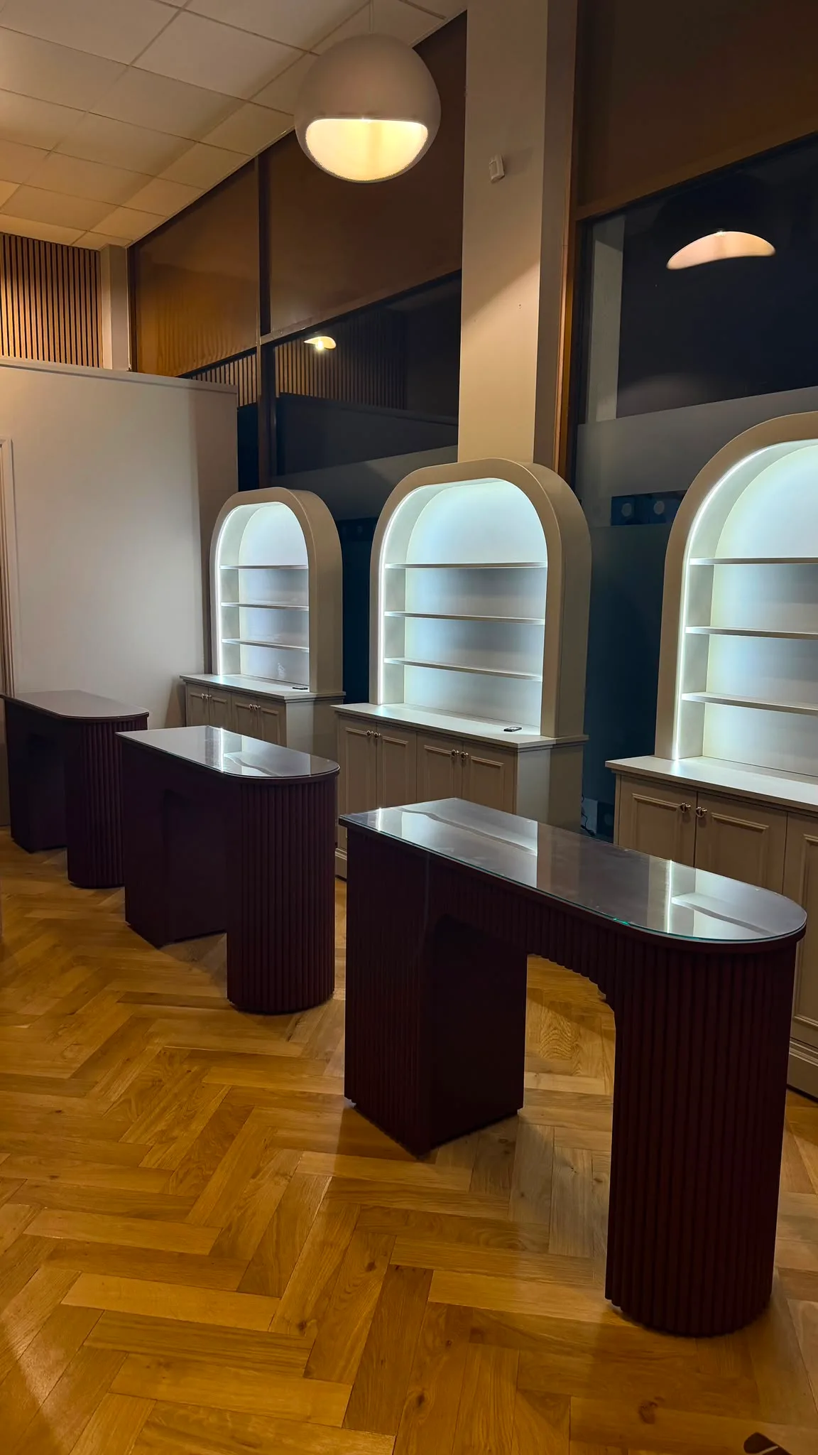 Row of three cabinets with curved bookcases and integrated LED lighting, situated behind dark fluted manicure desks.