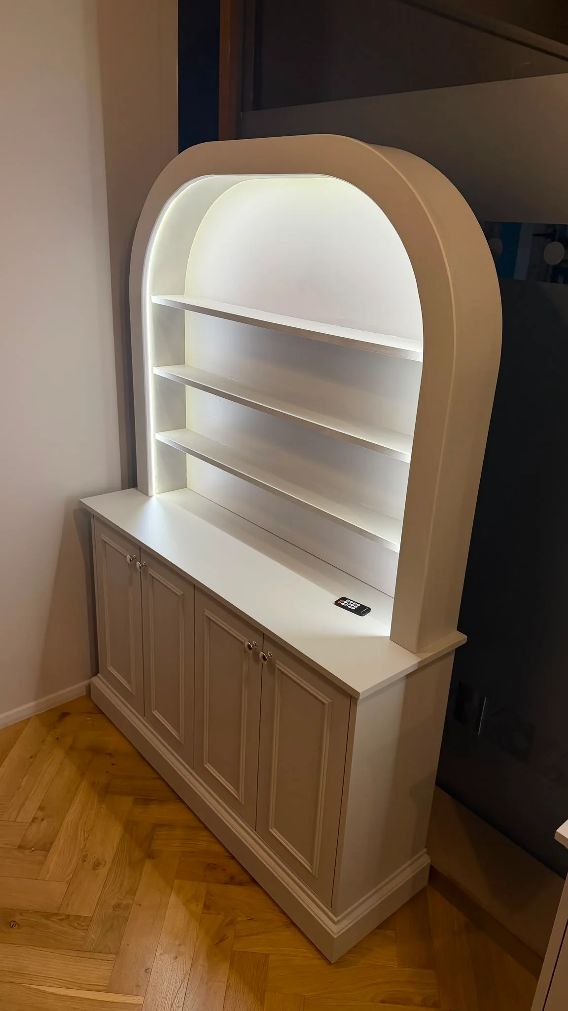 White cabinet with a curved bookcase featuring illuminated open shelving and classic panelled base storage.