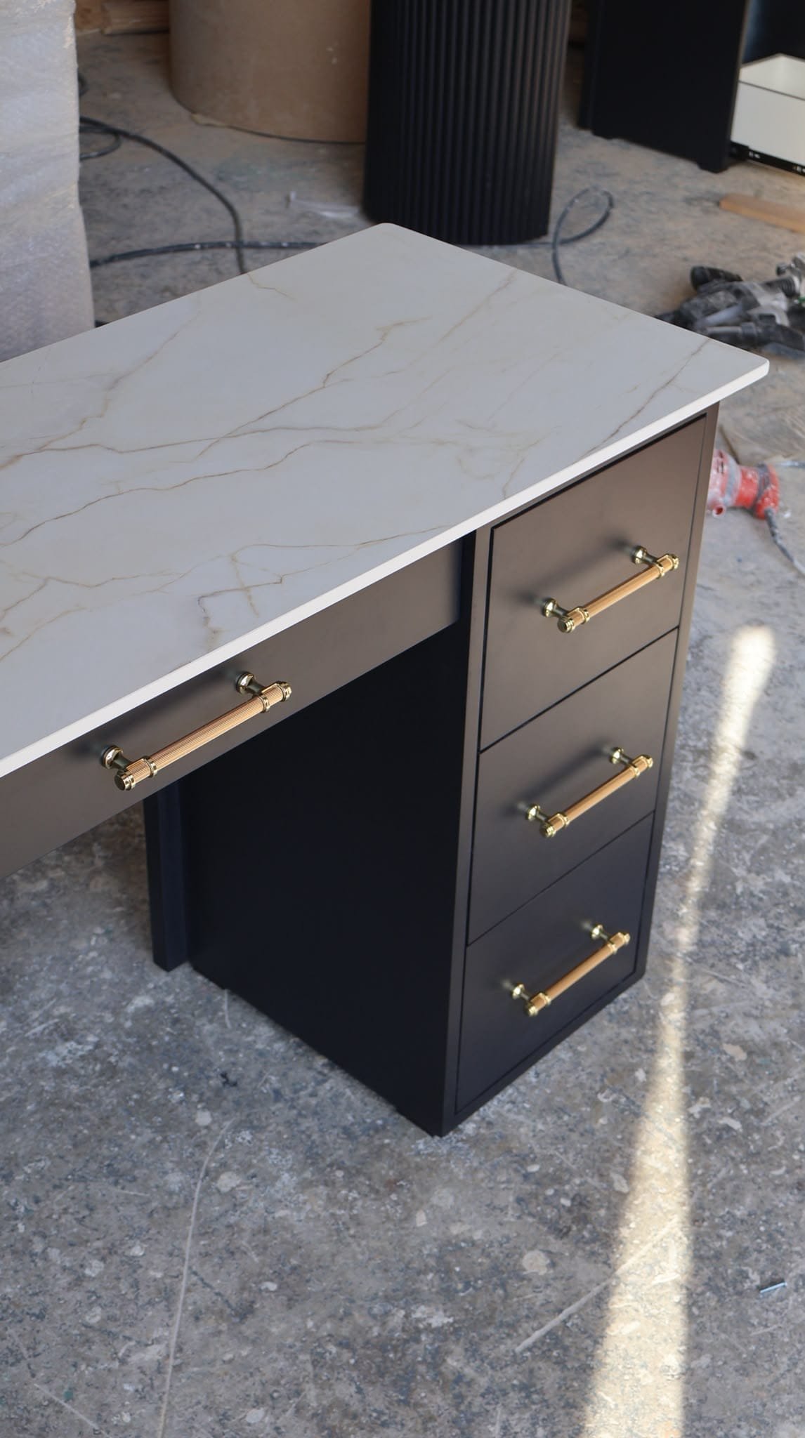 Close-up of black fluted salon desk showing the three-drawer pedestal with gold and wood-accent hardware and marble-effect worktop