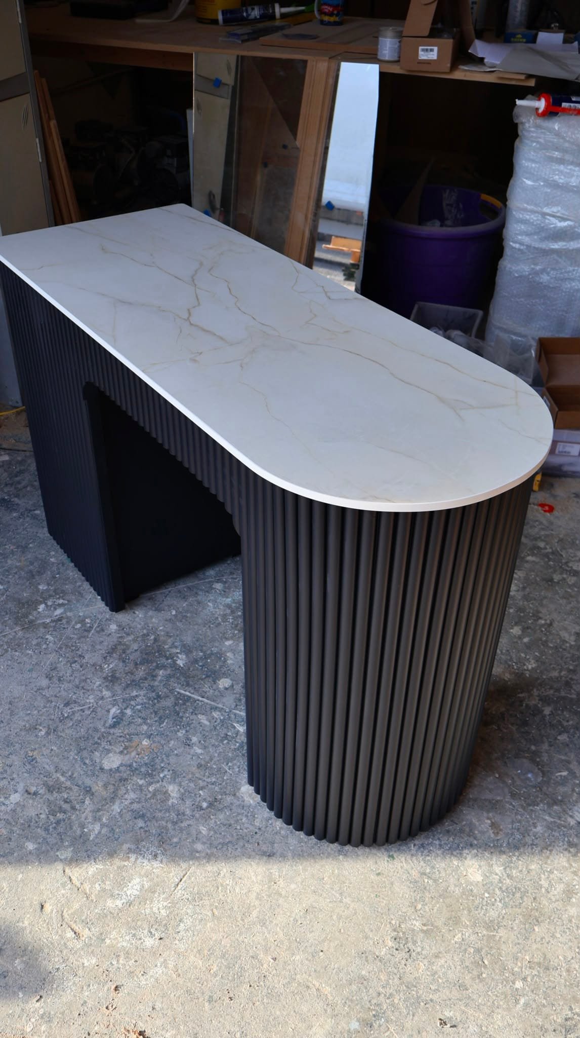 Bespoke black nail and beauty desk with curved fluted column support, marble-effect top, and integrated storage drawers in a UK workshop