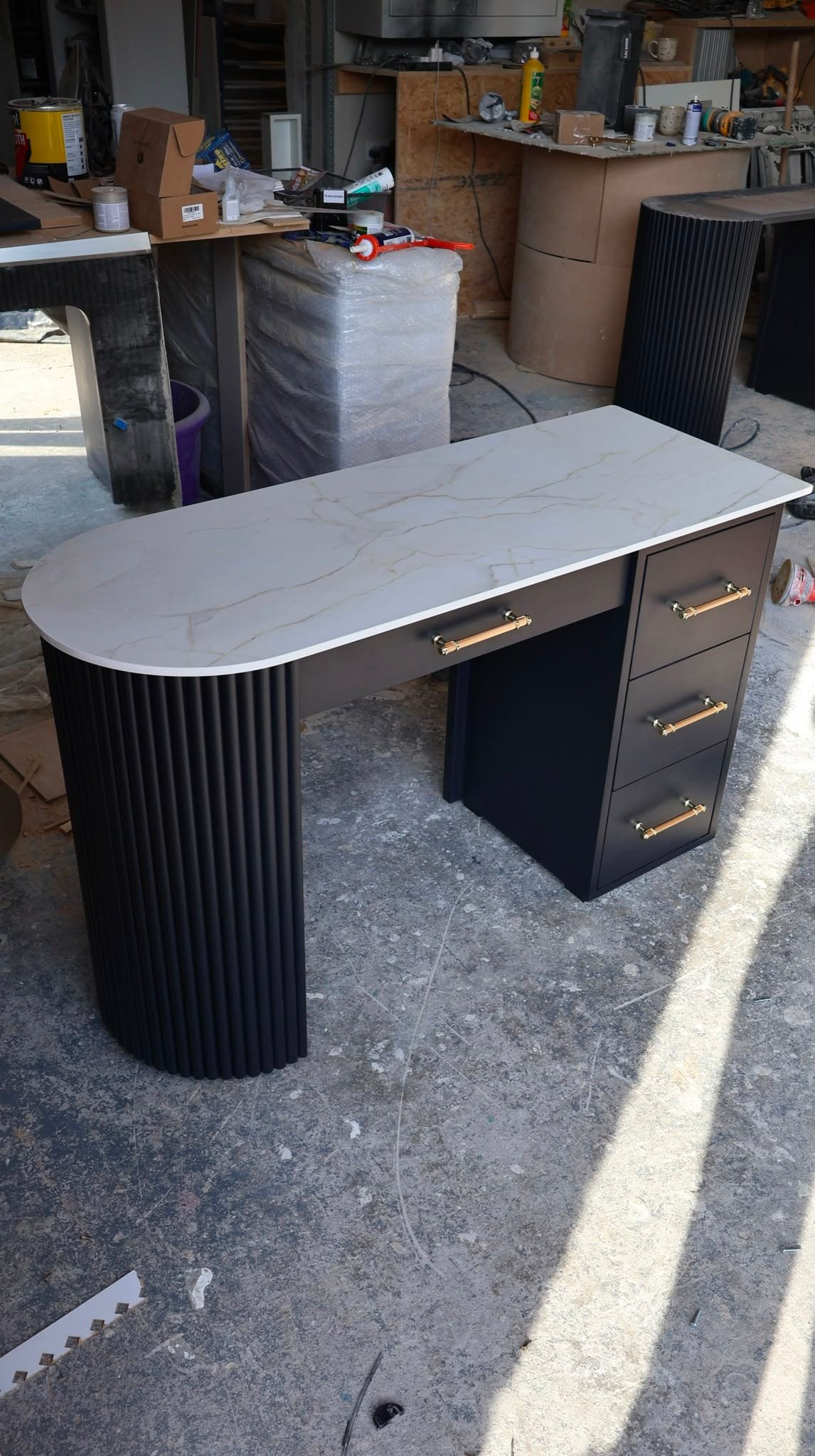 black bespoke salon desk with fluted curved end, marble-effect top, and gold and wood-accent drawer pulls